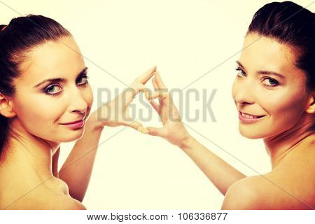 Two beautiful women making heart with fingers.