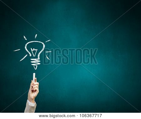 Human hand darwing light bulb as idea concept with chalk