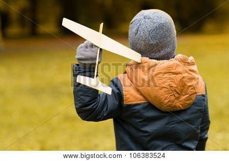 autumn, childhood, dream, leisure and people concept - happy little boy playing with wooden toy plane outdoors from back