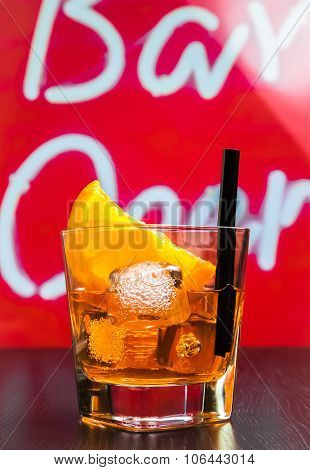 Glass Of Spritz Aperitif Aperol Cocktail With Orange Slices And Ice Cubes On Bar Table, Disco Atmosp