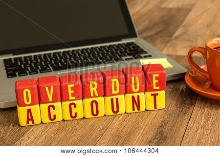 Overdue Account written on a wooden cube in front of a laptop