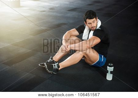 Sportsman wearing blue shorts and black t-shirt sitting on the floor in gym