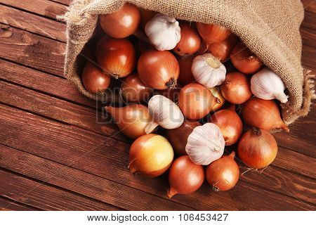 Scattered sac with fresh onions and garlic on wooden background