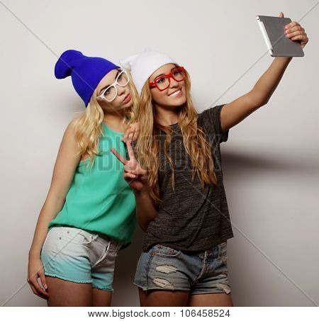 two hipster girls friends taking selfie with digital tablet, studio shot over gray vackground