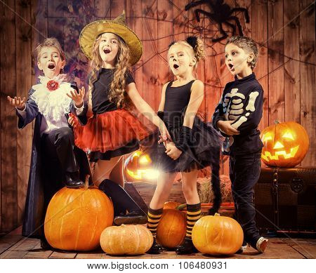 Cheerful children in halloween costumes celebrating halloween in a wooden barn with pumpkins. Halloween concept.