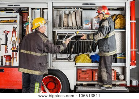 Mature and young firefighters working at truck in fire station