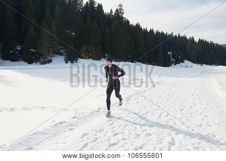 young  man jogging on snow in forest, bautiful sunny winter day. handsome sporty ahtlete man running
