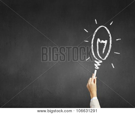 Human hand darwing light bulb as idea concept with chalk