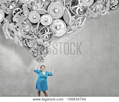 Stout woman of middle age pointing at gears mechanism