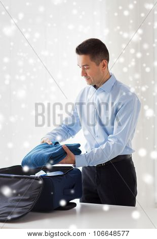 business, trip, luggage and people concept - happy businessman packing clothes into travel bag over snow effect over snow effect