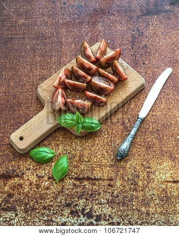 Ripe kumato tomatoes, basil leaves and knife on a rustic wooden chopping board over grunge rusty met