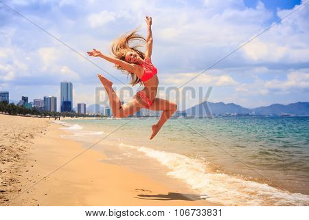 Blonde Slim Gymnast In Bikini In Jump Over Beach Against Sky
