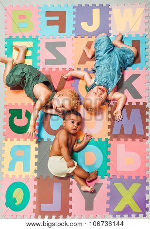 Multiethnic babies lying around on  Alphabet puzzle background