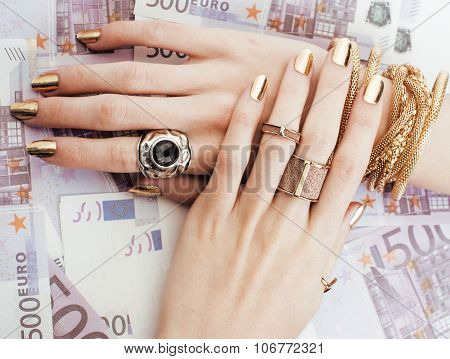 hands of rich woman with golden manicure and many jewelry rings on cash euros close up
