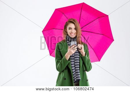Portrait of a smiling woman holding smartphone under umbrella and looking at camera isolated on a white background