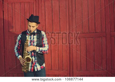 Handsome happy man in hat plays music on sax in front of red wooden background