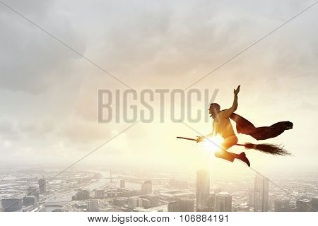Young businessman flying high above city on broom