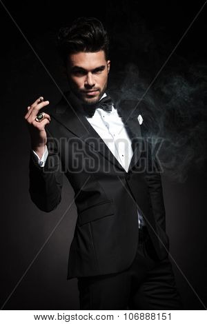 Handsome young business man enjoying a cigarette while holding one hand in his pocket.