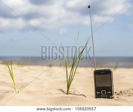 phone with long antenna receives a signal on a sandy beach