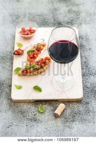 Wine appetizer set. Glass of red wine, brushettas with fresh tomato and basil on over rustic grunge