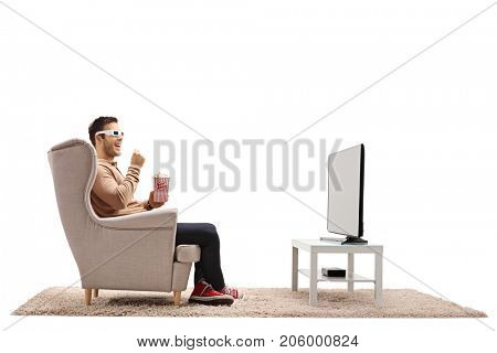 Young man with 3D glasses and popcorn sitting in an armchair and watching television isolated on white background