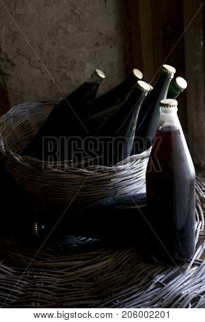 old and dusty botlles of aged red wine in a wicker basket illumined through a window
