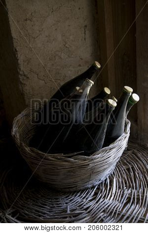 old and dusty botlles of aged red wine in a wicker basket illumined through a window