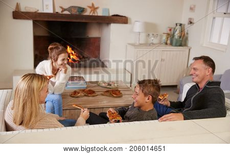 Family Sitting On Sofa In Lounge Next To Open Fire Eating Pizza