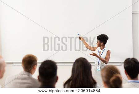 business, education and people concept - smiling african american businesswoman or teacher with marker showing something on screen to group of students at conference presentation or lecture