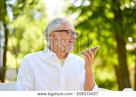 technology, senior people and communication concept - old man using voice command recorder or calling on smartphone at summer park