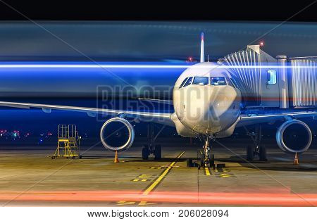 Modern white passenger airplane standing on parking place at night and get ready for boarding passengers at international airport.