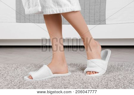 Woman standing in white spa slippers on grey fuzzy carpet