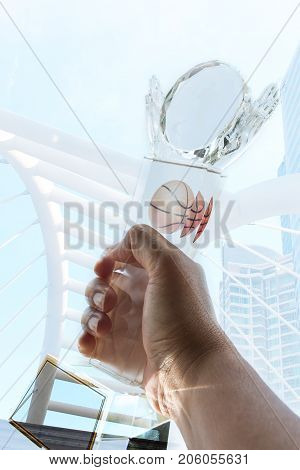 Businessman hands raised and holding light trophy design with basketbal show successful about sport against modern building background. Concept of Winners success award and appreciation.