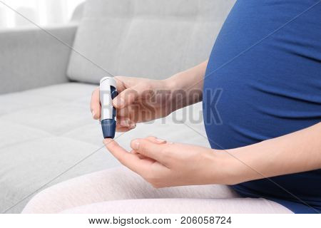 Pregnant woman taking blood sample with lancet pen indoors