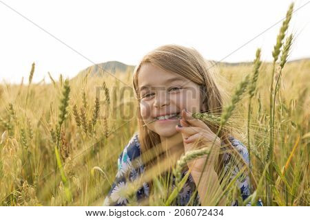 An Adorable little girl playing in the wheat field on a warm summer day