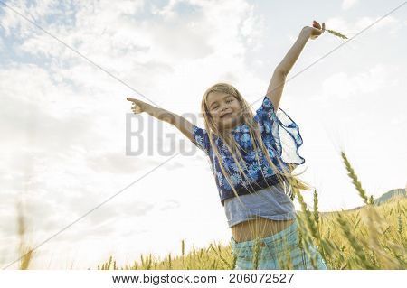 An Adorable little girl playing in the wheat field on a warm summer day