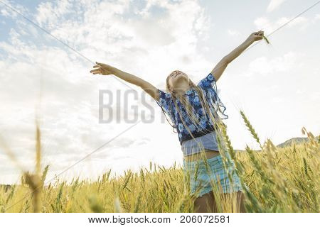 An Adorable little girl playing in the wheat field on a warm summer day