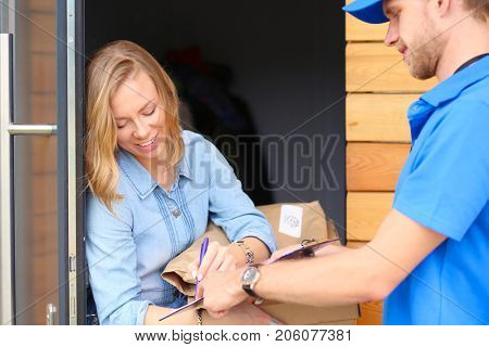 Smiling delivery man in blue uniform delivering parcel box to recipient - courier service concept. Smiling delivery man in blue uniform
