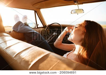 Image from car of pleased brunette woman lying on seat with closed eyes