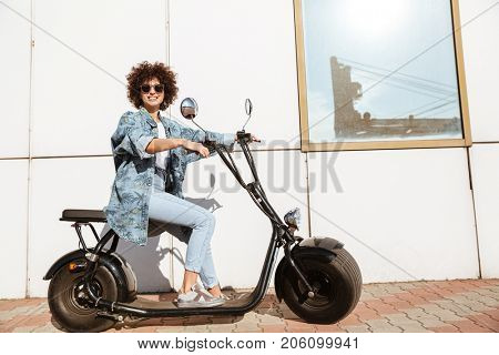 Stylish young woman sitting on a modern motorbike and looking at camera outdoors
