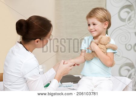 Cute smiling boy at the doctor with his little toy friend, not affraid to visit pediatrician, happy healthy childhood