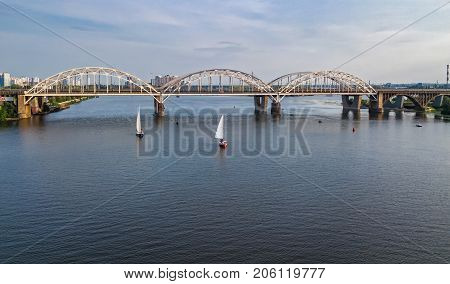 Aerial top view of Darnitsky bridge, yachts and boats sailing in Dnieper river from above, Kiev (Kyiv) city skyline, Ukraine