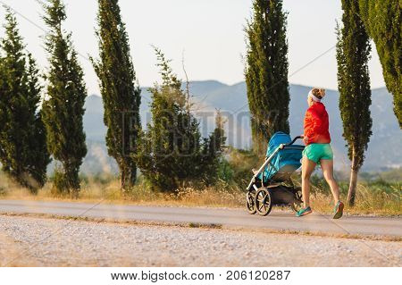 Running mother with child in stroller enjoying motherhood at sunset and mountains landscape. Jogging or power walking woman with pram on at sunset. Beautiful inspirational mountains landscape.