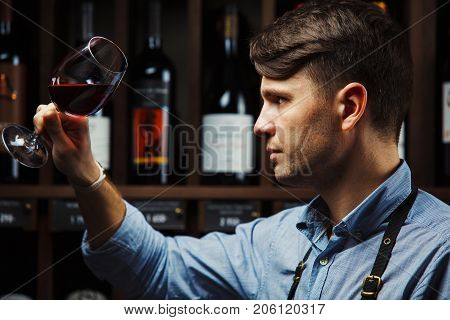 Bokal of red wine on background of male sommelier appreciating color, quality, flavor and sediments of drink. Professional degustation expert in winemaking.