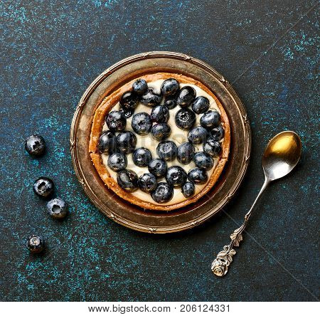 Blueberry tart, pie, tartlet with custard on blue stone background.