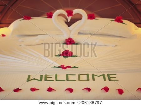 Floral decor, towel swans and word WELCOME on bed in hotel room