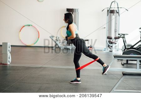 cute fit girl performs modern leg exercises with elastic rubber