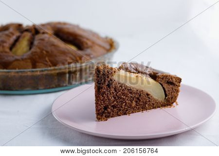 Slice of pear pie on pink plate with whole baked pie in background