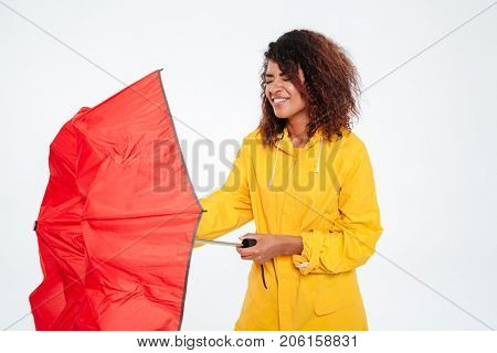 Confused african woman in raincoat close umbrella over white background