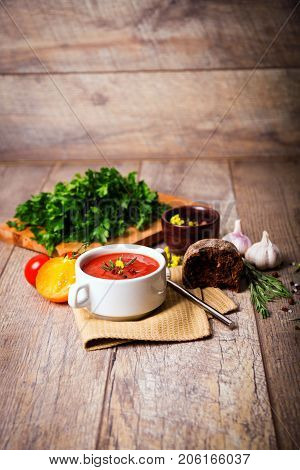 Red ukrainian borsch with sour, garlic, parsley, spices and a lot of dill and parsley on a wooden background. Copy space. Close-up of appetitzing dish. Food concept.
